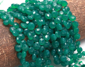 Puede incluir: Un hilo de cuentas de piedra preciosa verde en forma de corazón, facetadas y con acabado pulido. Las cuentas están ensartadas en un racimo denso, con un tono esmeralda vibrante y un corte uniforme. Dos borlas de tela verde con detalles plateados.