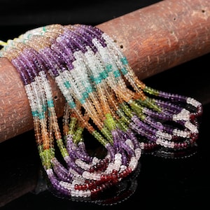 May include: Multiple strands of faceted gemstone beads in a variety of colors including purple, clear, teal, orange, green, and deep red. The small, round, disc-shaped beads are strung together in long, flowing lines that drape over a textured brown surface.