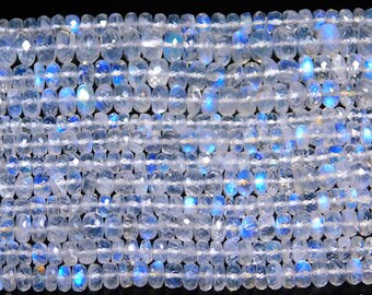May include: A strand of faceted, translucent moonstone beads arranged in multiple parallel rows. Each small, circular bead features a polished surface that reflects light, displaying a distinct blue adularescence or glow against a dark background.