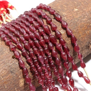 May include: A collection of deep red, translucent, teardrop-shaped beads strung together on multiple strands. The beads have a smooth, polished finish and are arranged in parallel lines, showcasing a consistent dark crimson hue throughout the set.