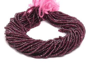 May include: A circular strand of small, faceted, deep red garnet beads arranged in a continuous loop. The beads are strung together and secured at the top with a bright pink thread, creating a contrast between the dark red stones and the vibrant pink.