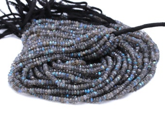 May include: A long strand of faceted labradorite beads in shades of grey, featuring iridescent blue and gold flashes. The beads are strung on a black cord that is tied into a tassel at one end, creating a dense, coiled arrangement of small stones.