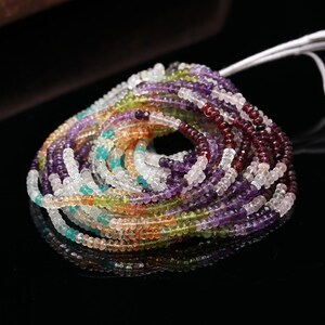May include: A coiled strand of small, faceted gemstone beads in a variety of colors including deep red, purple, light green, blue, and clear white. The beads are strung on a thin white cord, creating a circular arrangement with a central opening.