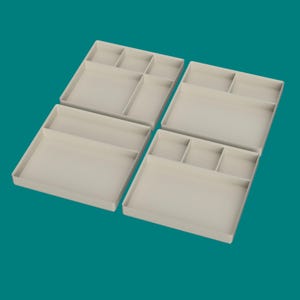 以下が含まれることがあります： 複数のコンパートメントを備えた、4つのベージュ色のプラスチック製オーガナイザートレイ。各トレイは長方形で、さまざまなサイズの収納セクションがあります。トレイは、ターコイズブルーの背景に斜めに配置されています。