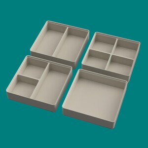 以下が含まれることがあります： ベージュ色のプラスチック製オーガナイザー用トレイ4つ。それぞれコンパートメントの構成が異なり、2つの仕切りがあるもの、3つ、4つ、そして1つのオープンなトレイがあります。トレイは、ターコイズブルーの背景に配置されています。