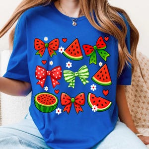 May include: A royal blue t-shirt with a watermelon and bow pattern. The shirt features red, green and white watermelons, and red and white polka dot bows.