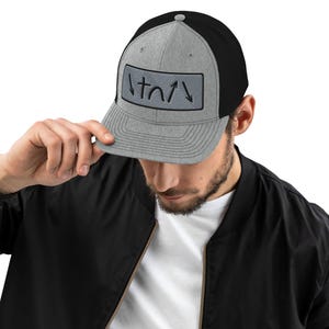 May include: A gray and black trucker hat with a black patch on the front that says "/t//" in black.