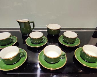 May include: A set of six green and gold teacups and saucers with a matching creamer. The cups and saucers have a gold rim and a green base.