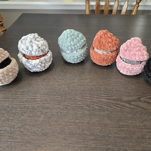 May include: Six crocheted, round, fabric containers with lids. The containers are in various colors, including beige, gray, blue, orange, pink, and black.
