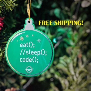 May include: A green Christmas bauble with the text "eat(); //sleep(); code();" on it. The bauble is hanging from a gold string on a Christmas tree.