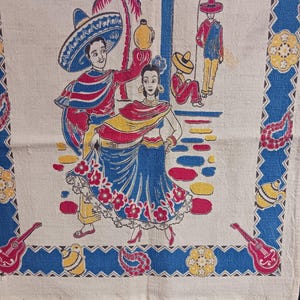 May include: A vintage kitchen towel with a colorful design featuring a couple dancing in traditional Mexican clothing. The scene is set against a backdrop of a palm tree, a building with an archway, and a blue sky. The towel has a blue and white border with a repeating pattern of flowers, musical instruments, and other decorative elements.