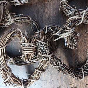 May include: Close-up of several handmade grapevine wreaths. The wreaths are made of intertwined brown vines and are tied together with thinner vines. The background is a dark wooden surface.