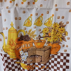 May include: White kitchen towel with a coffee-themed design. Features yellow coffee cups, a coffee pot, a bag of coffee beans, a coffee grinder, and a vase of yellow flowers. The bottom border has a brown and white checkered pattern.