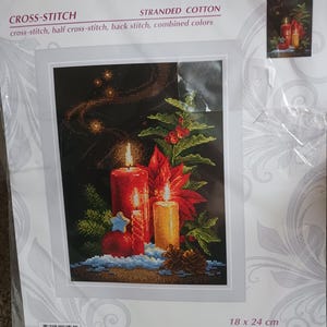 May include: A Riolis 2056 Christmas Light cross-stitch kit package featuring a design of red and yellow candles, holly, and a blue star on a black background. The packaging includes the text 18 x 24 cm and 7 x 9 1/2 inches.