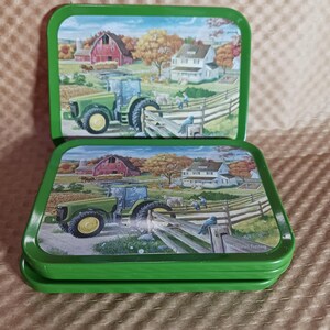 May include: Two green metal coasters with a rural scene featuring a green tractor, red barn, and white house. The coasters are stacked, showing the detailed artwork of a farm landscape.