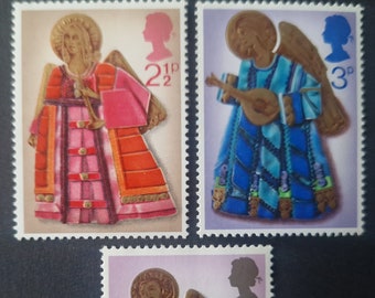 May include: Three vintage postage stamps featuring angels playing musical instruments. The stamps are from Great Britain and feature the denomination in pence: 2 1/2 pence, 3 pence, and 7 1/2 pence.