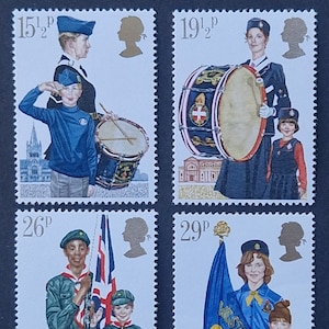 May include: Four vintage postage stamps featuring children in uniform with a drum, flag, and a woman in uniform. The stamps are from the United Kingdom and feature the text "15 1/2p", "19 1/2p", "26p", and "29p".