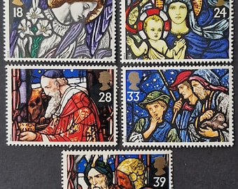 May include: A collection of five postage stamps featuring stained-glass artwork. The stamps depict religious figures, including an angel, the Virgin Mary with baby Jesus, and the three wise men. Each stamp has a different value, ranging from 18 to 39.