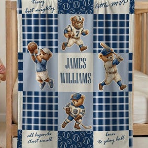 May include: A navy blue and white baby blanket with a sports theme. The blanket features teddy bears playing football, baseball, basketball, and hockey. The name "JAMES WILLIAMS" is displayed in the center. The blanket has the phrases "tiny but mighty", "all legends start small", and "born to play ball".