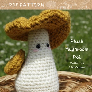 Puede incluir: Un juguete de peluche de hongo tejido a crochet con un cuerpo blanco y una tapa amarilla. El hongo tiene una cara linda con ojos negros y mejillas rosadas. El texto "Plush Mushroom Pal" y "Pattern by Ellen Cerrone" es visible en la imagen.