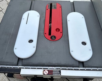 May include: A table saw with three white plastic inserts and a red insert with a slot in the center. The table saw has a ruler with markings in inches.