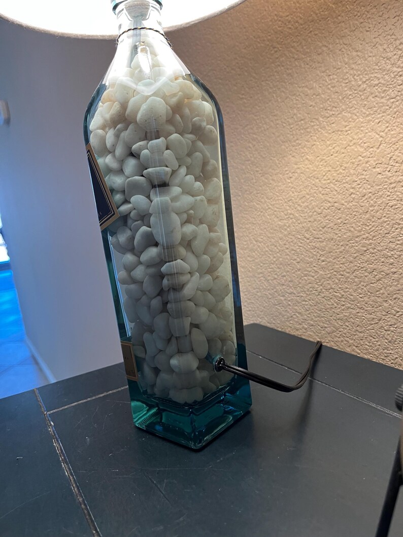 May include: A clear glass bottle lamp with white rocks inside. The bottle is blue at the bottom and has a black cord.