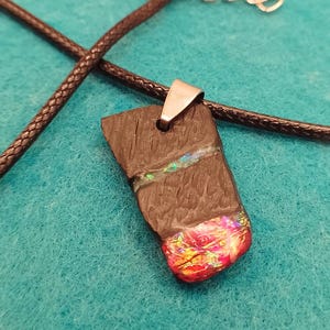 Può includere: Un ciondolo nero con una balla d'argento e un'intarsio iridescente colorato. Il ciondolo è su una collana di cordoncino nero.