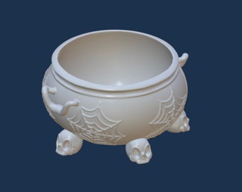May include: White ceramic cauldron with a spiderweb design and skull feet. The cauldron is perfect for Halloween decorations or candy storage.