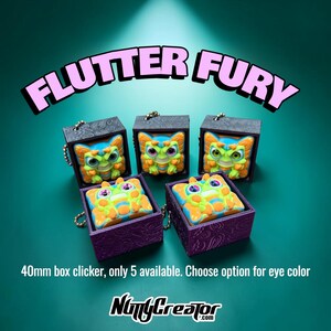 May include: Five 40mm square box clickers labeled FLUTTER FURY. Each features a colorful creature with orange and green patterns and distinct eye colors inside a textured black or purple box with a metal chain attachment. NuttyCreator.com logo.