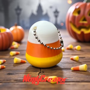 May include: A candy corn-shaped keychain with white, orange, and yellow stripes. The keychain has a silver ball chain and is surrounded by miniature pumpkins and candy corn pieces. The background features a spooky Halloween scene.