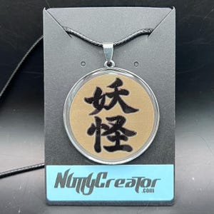 Yokai in Japanese Kanji engraved pendant necklace, light gold background, stainless steel, about 1.5 inches in diameter.