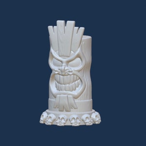 Peut inclure: Une statue tiki blanche avec un visage en colère et une rangée de crânes à la base. La statue a une texture de bois sculpté et un design stylisé, idéal pour la décoration tropicale ou fantaisie.