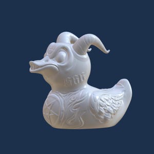 May include: White rubber duck with a demonic design, including horns, wings, and a pentagram. The duck has a detailed, textured surface and the word "GRILL" is inscribed on its chest.