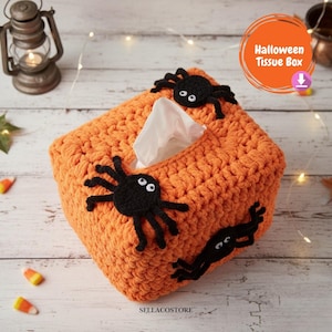 May include: Orange crocheted tissue box cover decorated with three black spiders. The tissue box has a rectangular shape and a slot for tissue dispensing. The text "Halloween Tissue Box" is in a circle on the top right.
