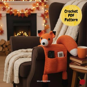 Könnte beinhalten: Ein gehäkelter, orangefarbener Fuchs-Organizer mit zwei Taschen, schwarzen Pfoten und einem weißspitzigen Schwanz. Der Fuchs sitzt auf der Armlehne eines braunen Stuhls. Der Text "Crochet PDF Pattern" befindet sich in einem gelben Kreis. Der Text "SELLLACOSTORE" steht unten.