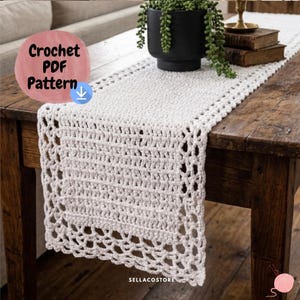 May include: A white crochet table runner with a detailed openwork design. The runner is displayed on a dark wooden table, with a plant and books in the background. The text "Crochet PDF Pattern" is visible in the image.
