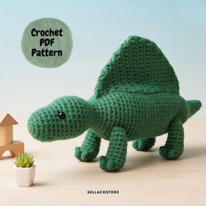 May include: A green crocheted dinosaur toy with a large dorsal fin. The dinosaur has small black eyes and is positioned on a light-colored surface. A green circle with the text "Crochet PDF Pattern" is in the upper left corner.