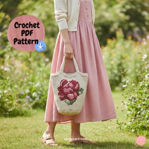 May include: A cream-colored crochet tote bag with a floral design in shades of red and pink. The bag is held by a person wearing a pink dress and a cream-colored cardigan. The image also includes the text "Crochet PDF Pattern".