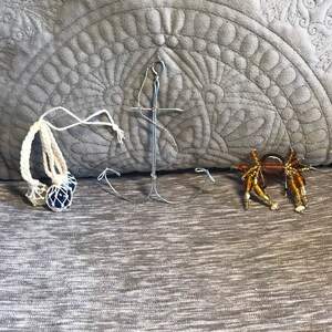 May include: Three nautical themed ornaments: a white rope with blue glass balls, a silver anchor, and a beaded crab with brown, orange, and white beads.
