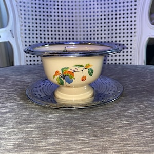 Puede incluir: Un tazón de cerámica blanca con un borde plateado y un diseño floral. El tazón está sobre un plato plateado con un borde decorativo.