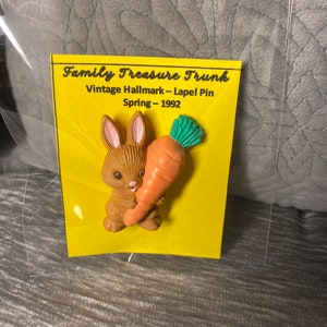 May include: A vintage Hallmark lapel pin from 1992 featuring a brown bunny holding an orange carrot with green leaves. The pin is on a yellow card with the text "Family Treasure Trunk".