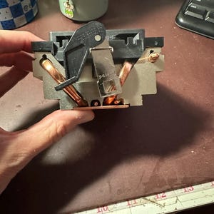 Könnte beinhalten: Ein Computer-CPU-Kühler mit einem silberfarbenen Metall-Kühlkörper und freiliegenden Kupfer-Heatpipes. Die Einheit umfasst eine schwarze Kunststoff-Montagehalterung mit einem Metallhebelmechanismus und einem sichtbaren Patentstempel.