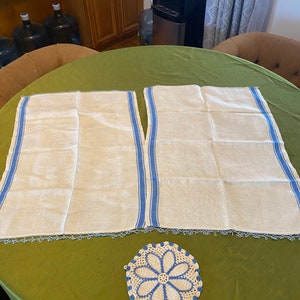 Puede incluir: Dos toallas de té de lino blanco con rayas azules y bordes de ganchillo, y un encaje de ganchillo blanco con ribete azul.
