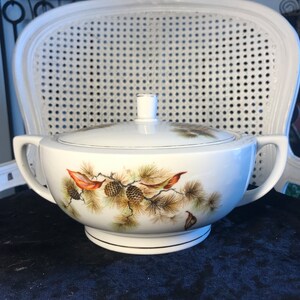 May include: White ceramic serving bowl with a lid, featuring a pine cone and branch design in shades of brown and green.