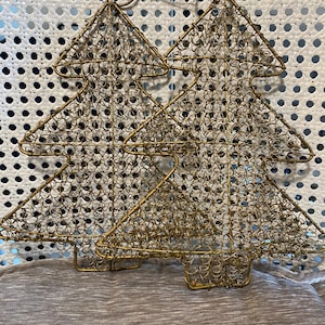 以下が含まれることがあります： 金色のワイヤーでできたクリスマスツリーのオーナメント2つ。ツリーは繊細なワイヤーメッシュでできており、ベースでつながっています。