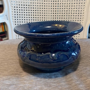 May include: A deep blue ceramic planter with a wide rim and a slightly rounded body. The planter has a glossy finish and subtle variations in the glaze.