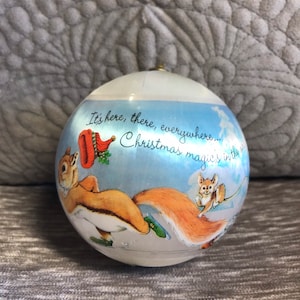May include: A white Christmas bauble with a blue background featuring a squirrel and a mouse ice skating. The bauble has the text "It's here, there, everywhere... Christmas magic's in the air."