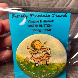 Puede incluir: Botón de Pascua vintage Hallmark con una niña con un vestido rosa y un delantal blanco, saltando por un campo de tulipanes amarillos y rosas. El botón dice "Happy Tulip Time" y está etiquetado como "Vintage Hallmark Easter Button Spring - 1978".