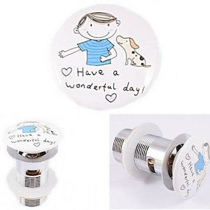 May include: White ceramic sink drain stopper featuring a cartoon illustration of a person and a dog, with the text "Have a wonderful day!" in black script. The stopper has a chrome metal base.