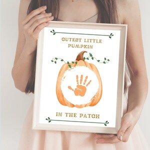 Könnte beinhalten: Ein druckbares Schild mit einem Aquarellkürbis und dem Text "Cutest Little Pumpkin in the Patch". Der Kürbis hat Platz für einen Handabdruck.